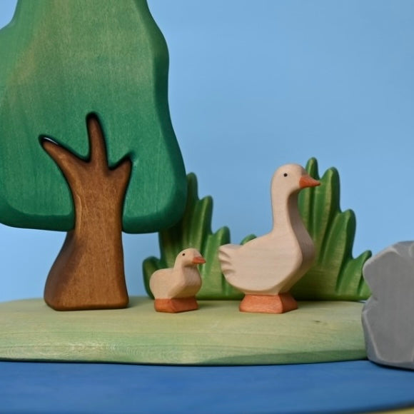 Wooden gosling beside larger geese in a small-world pond scene