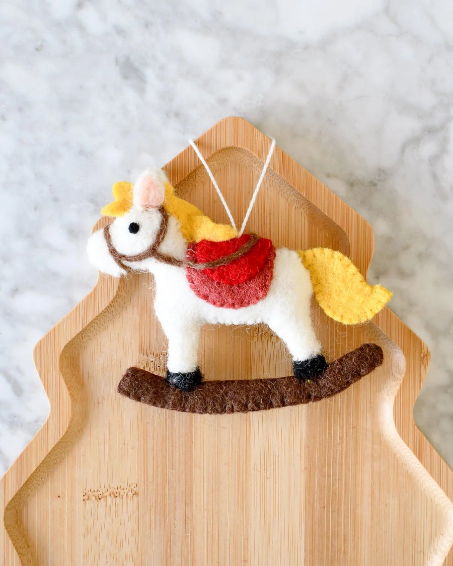 Felt Christmas rocking horse ornament with a golden mane, red saddle, and brown rocker, hanging from a white loop