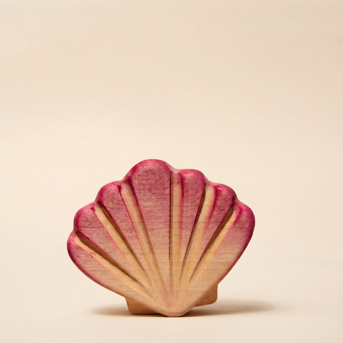 Wooden scallop shell painted pink, standing upright on sand