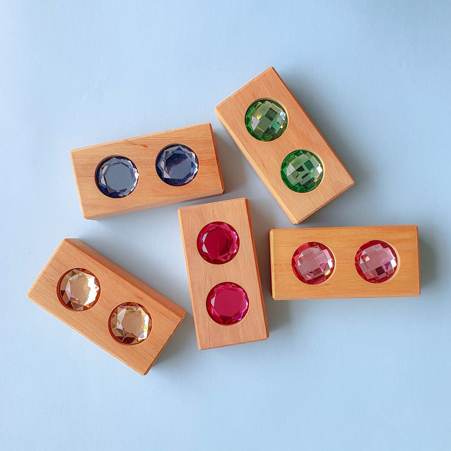 Five Bauspiel Color Track blocks with matching pairs of faceted gems in purple, green, red and gold