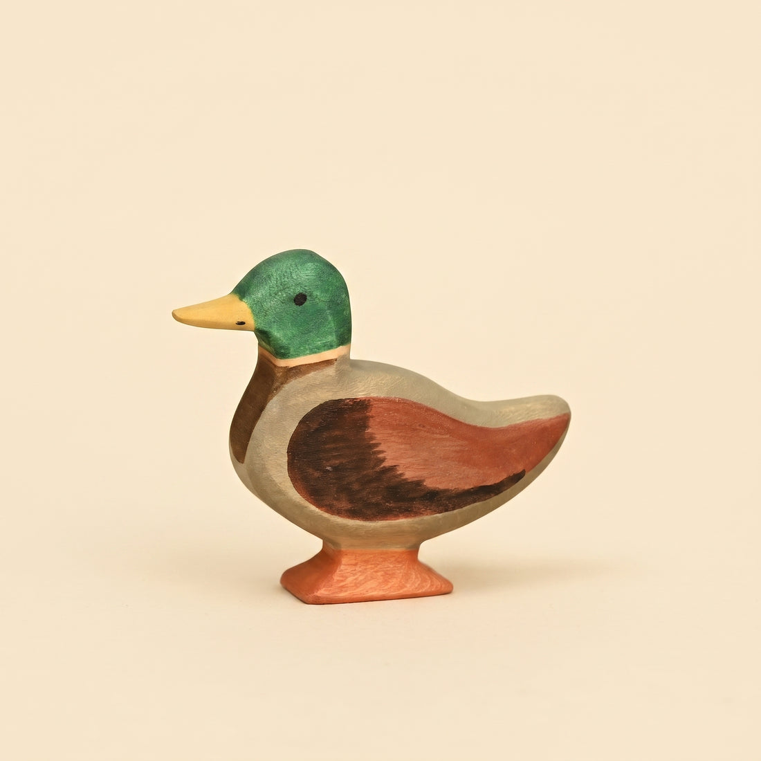 Wooden mallard duck figure with a green head, yellow bill, and chestnut wing, standing on an orange base
