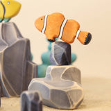 Wooden clown fish painted orange with white bands, beside a pale rock · view 1