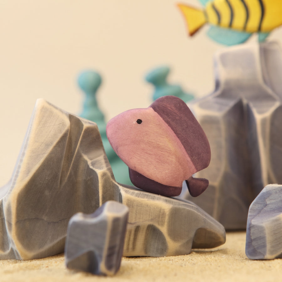 Wooden discus fish painted dusty pink, beside a pale rock