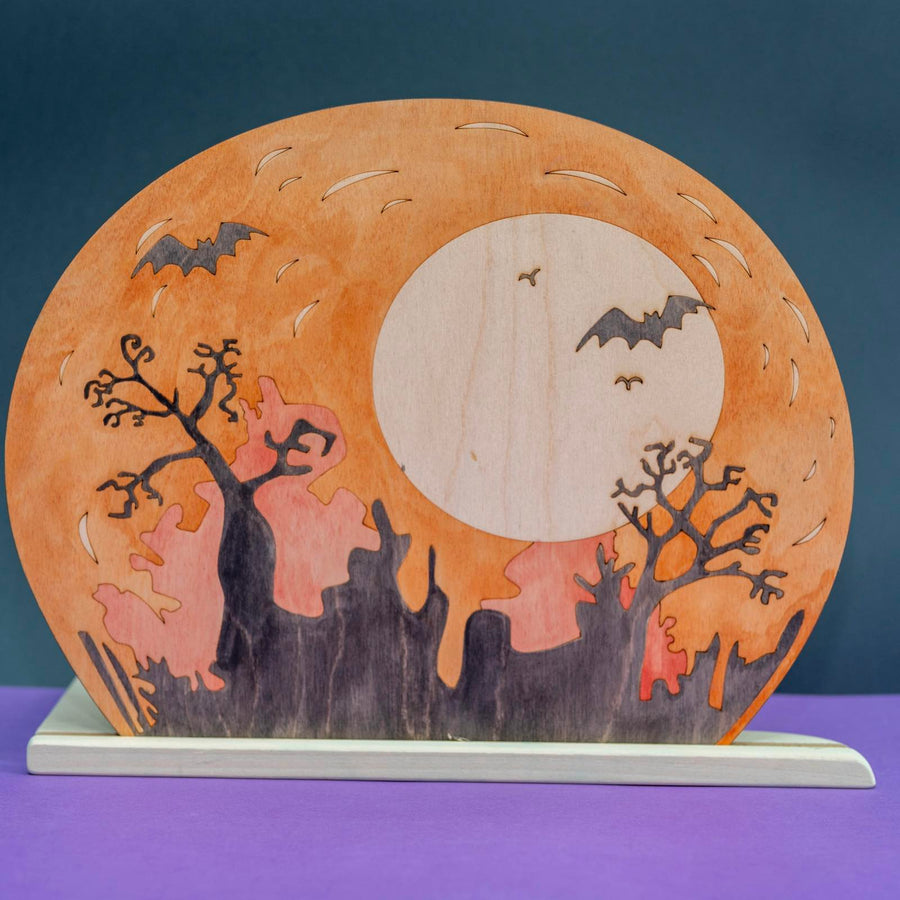 Wooden Halloween scene panel with a full moon, bats, and bare trees cut through the wood, on a standing base