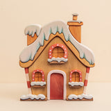 Wooden Christmas house with a snow-covered roof, a red door, and lit windows · view 1