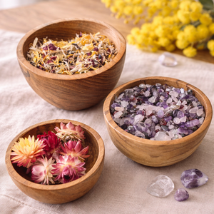Three graduated teak nesting bowls holding petals and stones