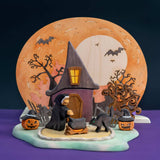 Wooden Halloween scene with a witch house, a full moon panel behind it, a fence, and small pumpkins · view 1