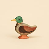 Wooden mallard duck figure with a green head, yellow bill, and chestnut wing, standing on an orange base · view 1