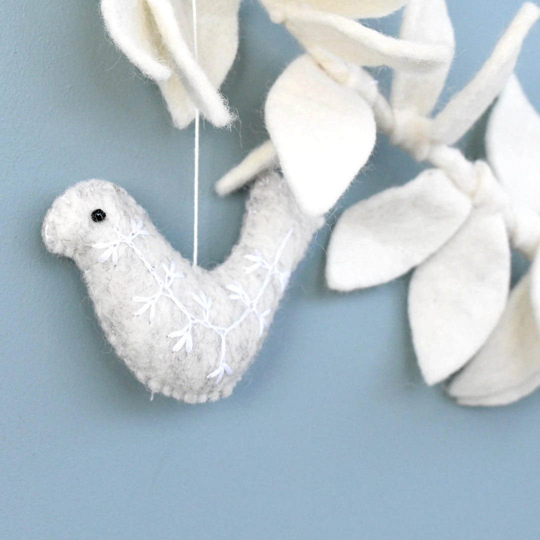 Close up of a grey felt dove with a white embroidered sprig and a small black bead eye, hanging from the cream leaf garland