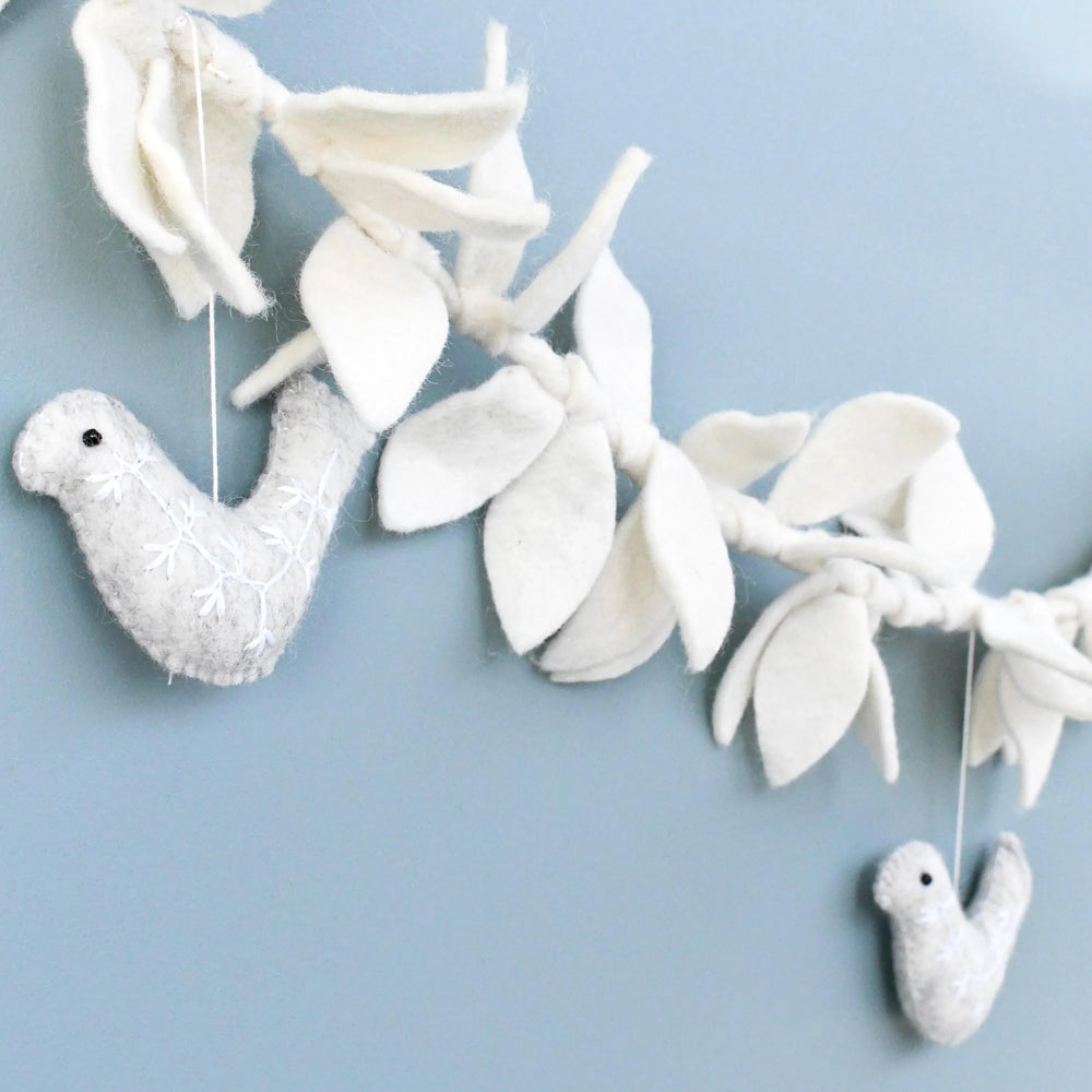 Felt doves and leaves garland strung along a wall, cream leaves knotted along a twisted cord with grey doves hanging below
