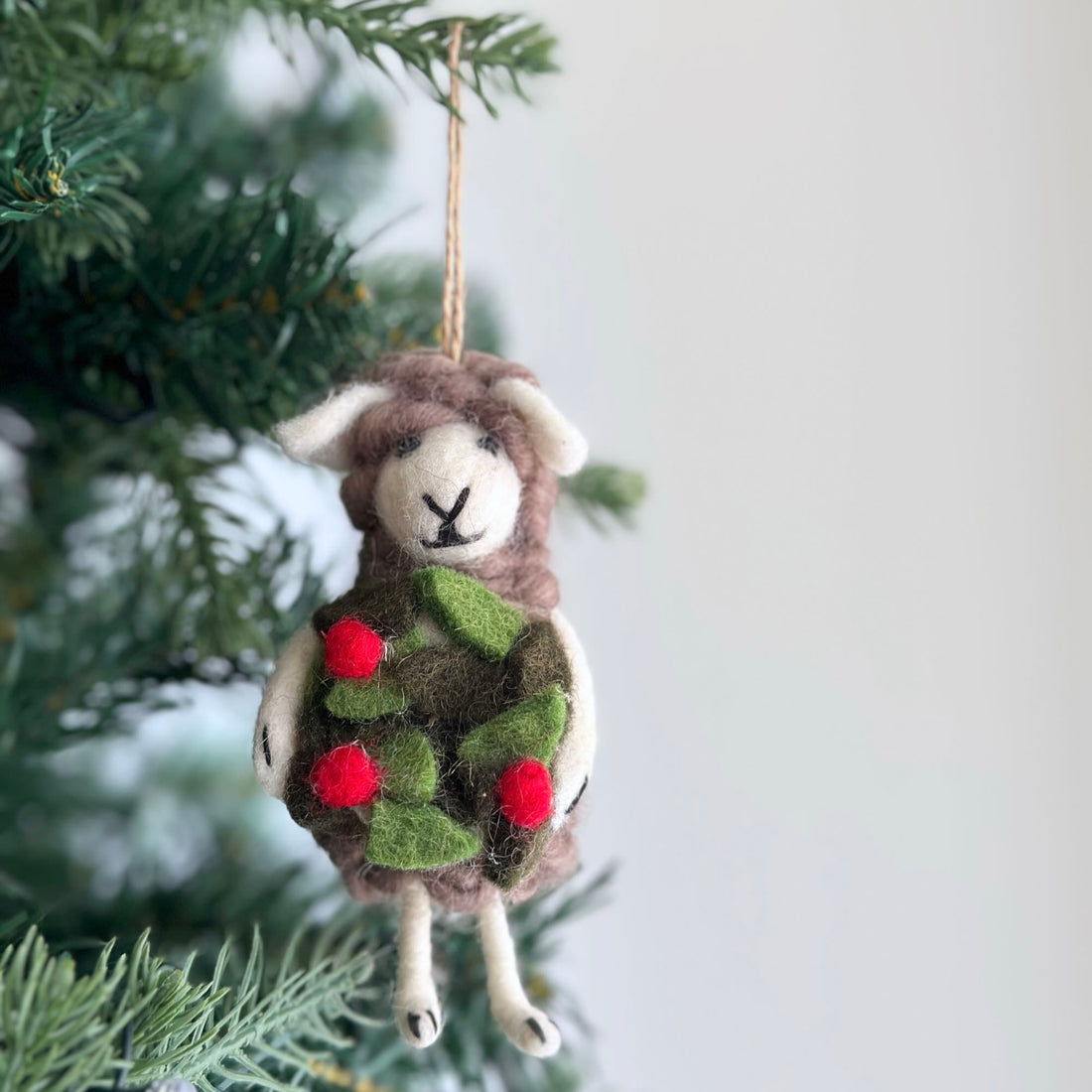 Holly-Wreath Holding Sheep Ornament, a wool felt ornament by Ganapati Crafts Co., needle-felted and hand-stitched in Nepal