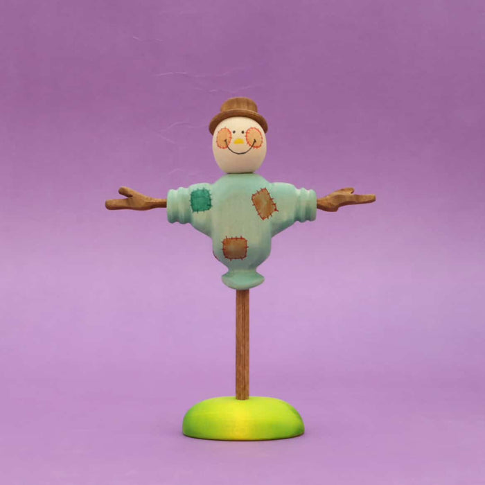 Wooden scarecrow with outstretched arms and a painted shirt, standing on a round base