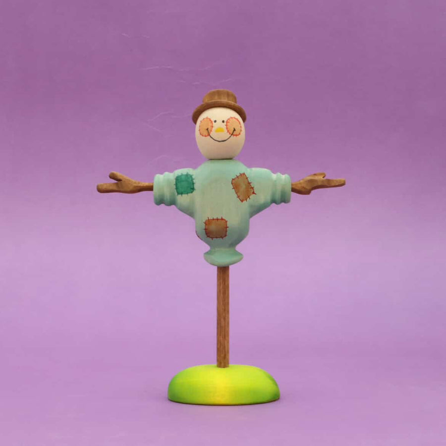 Wooden scarecrow with outstretched arms and a painted shirt, standing on a round base