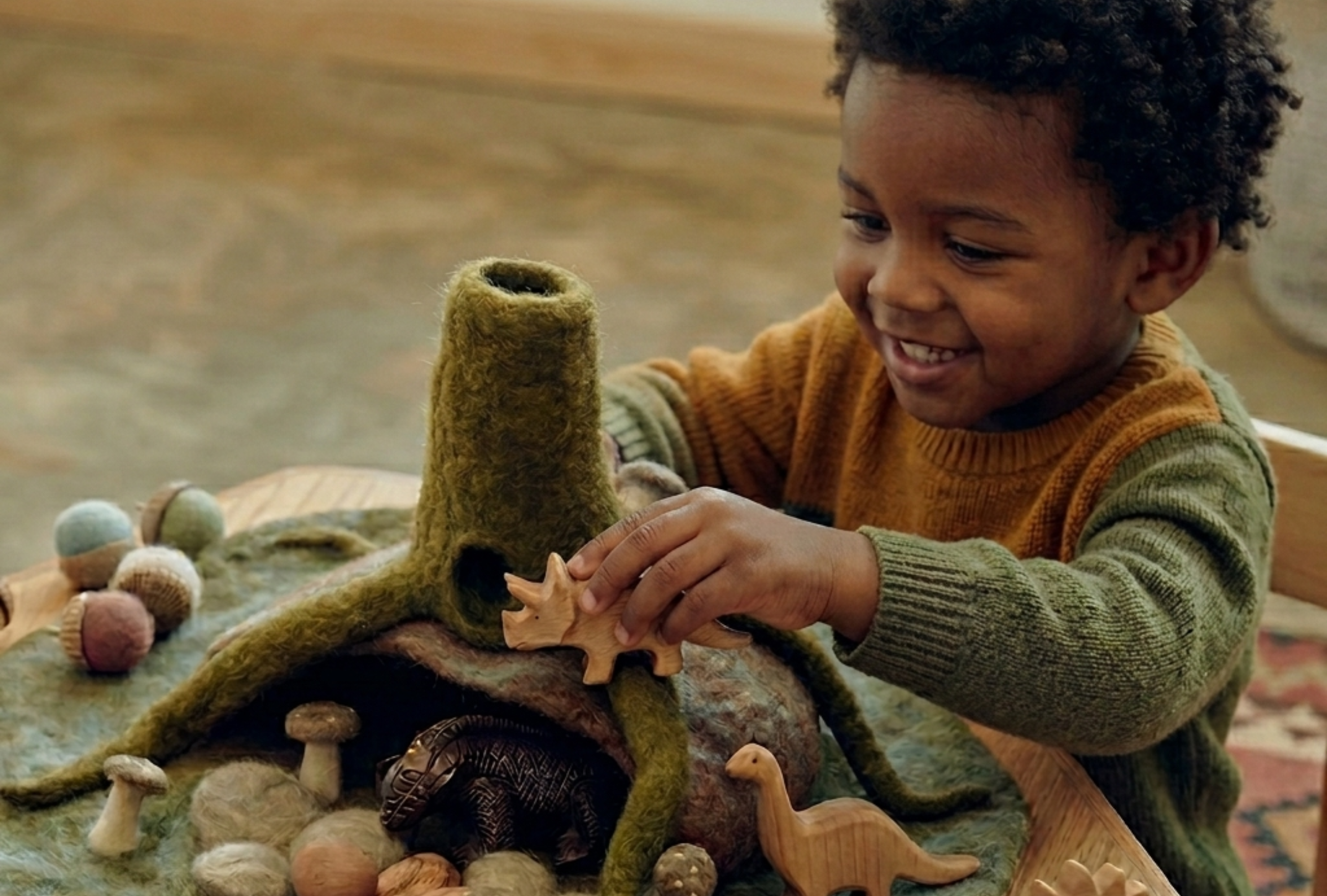 Felt figures arranged on the Papoose Forest Caves Play Mat, beside the lift-up mossy cave and felt acorns.
