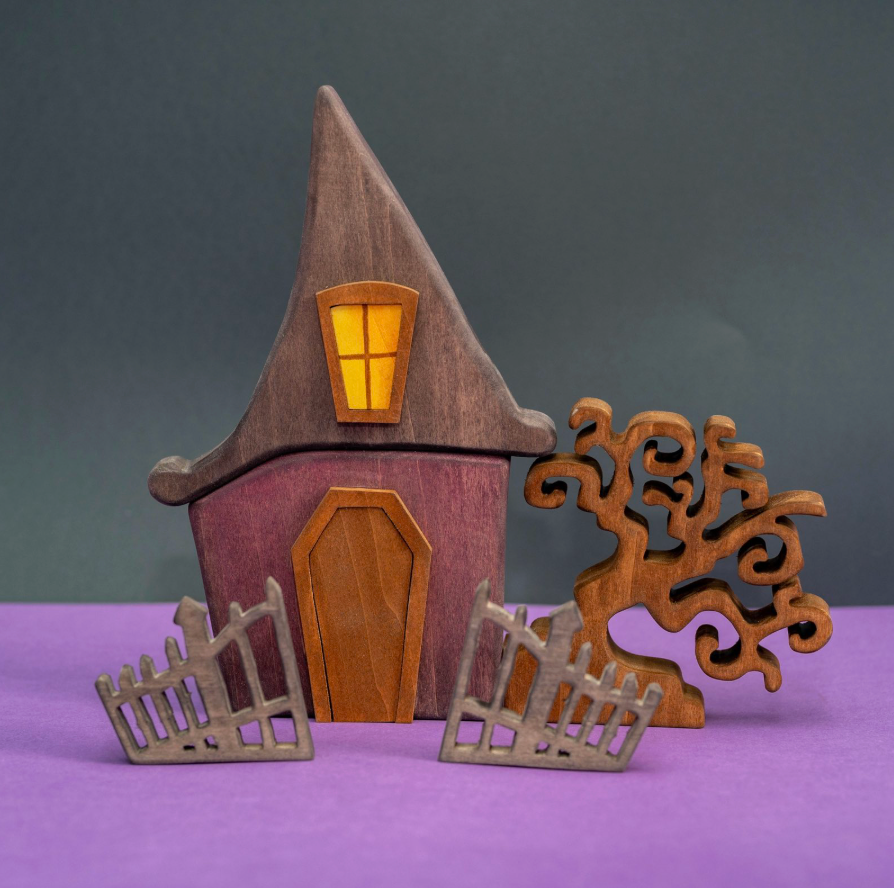 Wooden Halloween witch house with a tall pointed roof, a lit lantern above the door, and a curling bare tree at its side