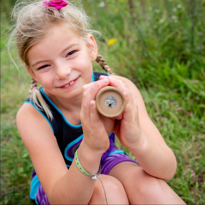 A young girl smiling and holding a kaleidoscope outdoors